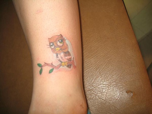 Cute cartoon owl perched on a branch ankle tattoo
