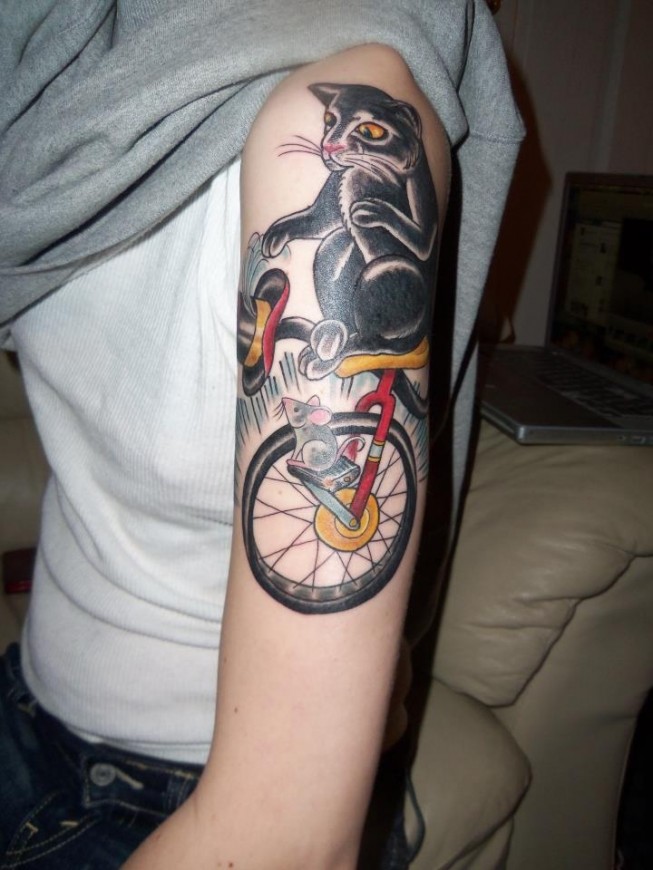 Girls cat and mouse on a unicycle tattoo on her arm