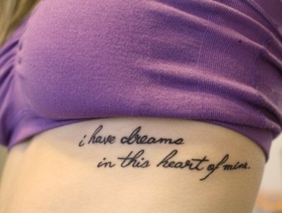 “i have dreams in this heart of mine.” quote tattoo on girls ribcage