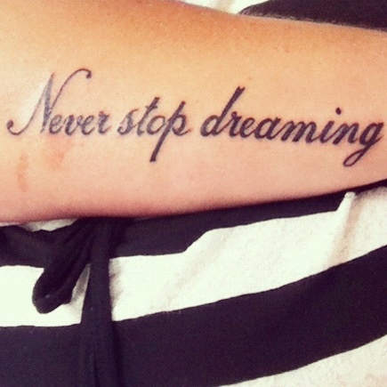 “Never stop dreaming” quote tattoo on girls arm